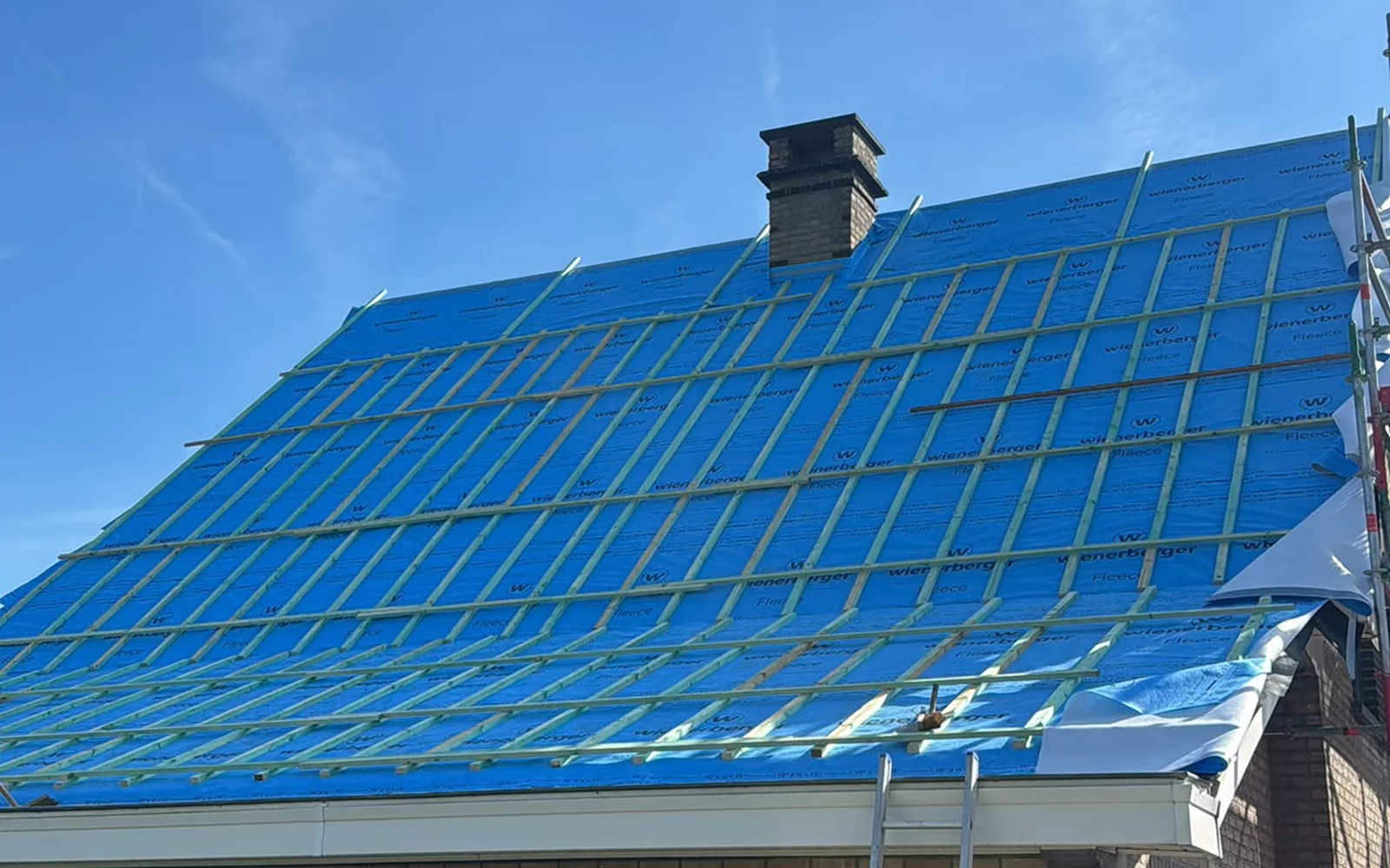 La même toiture pendant le chantier : ancienne couverture déposée, pare-pluie bleu et contre-lattage posés